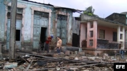 Dos hombres limpian escombros en una casa que ha sido parcialmente destruida por el paso del huracán "Sandy".